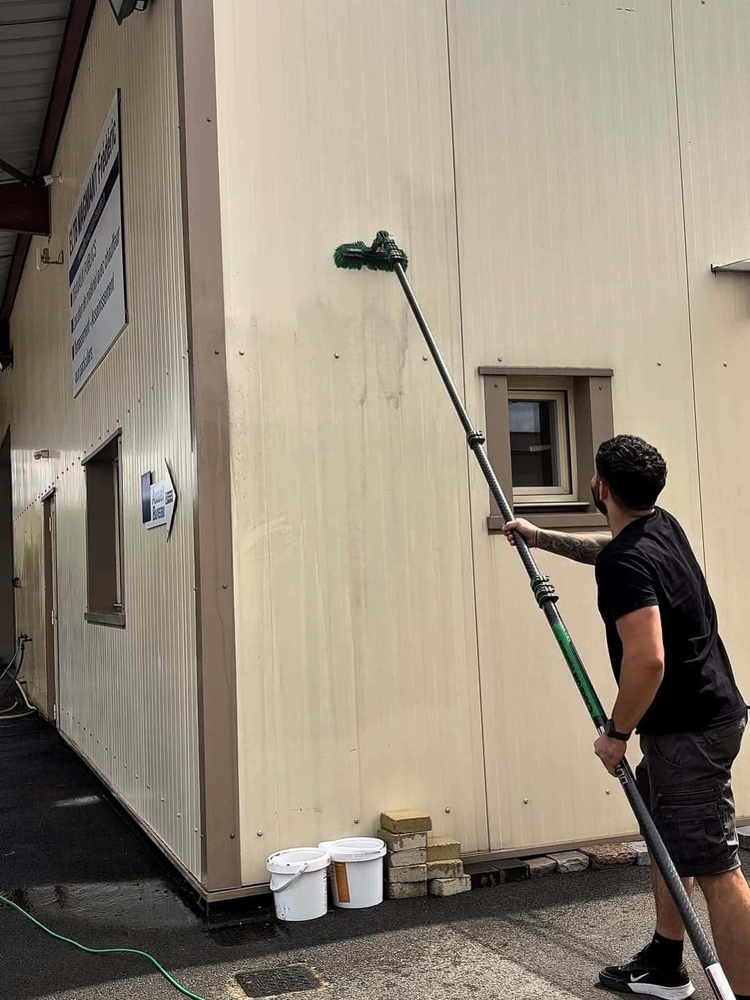Opérateur nettoyant un bardage industriel à la perche dans l'Aisne