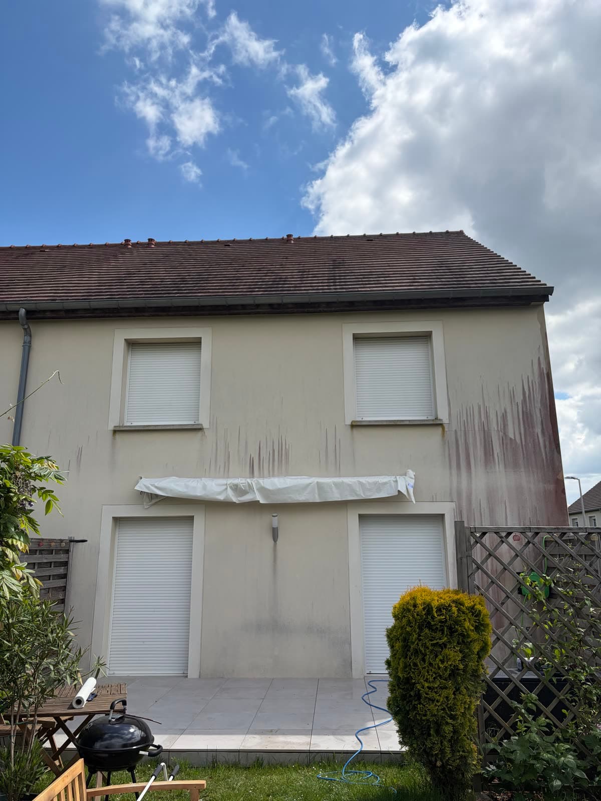 Façade arrière de maison marquée par des coulures rouges sous la toiture avant nettoyage