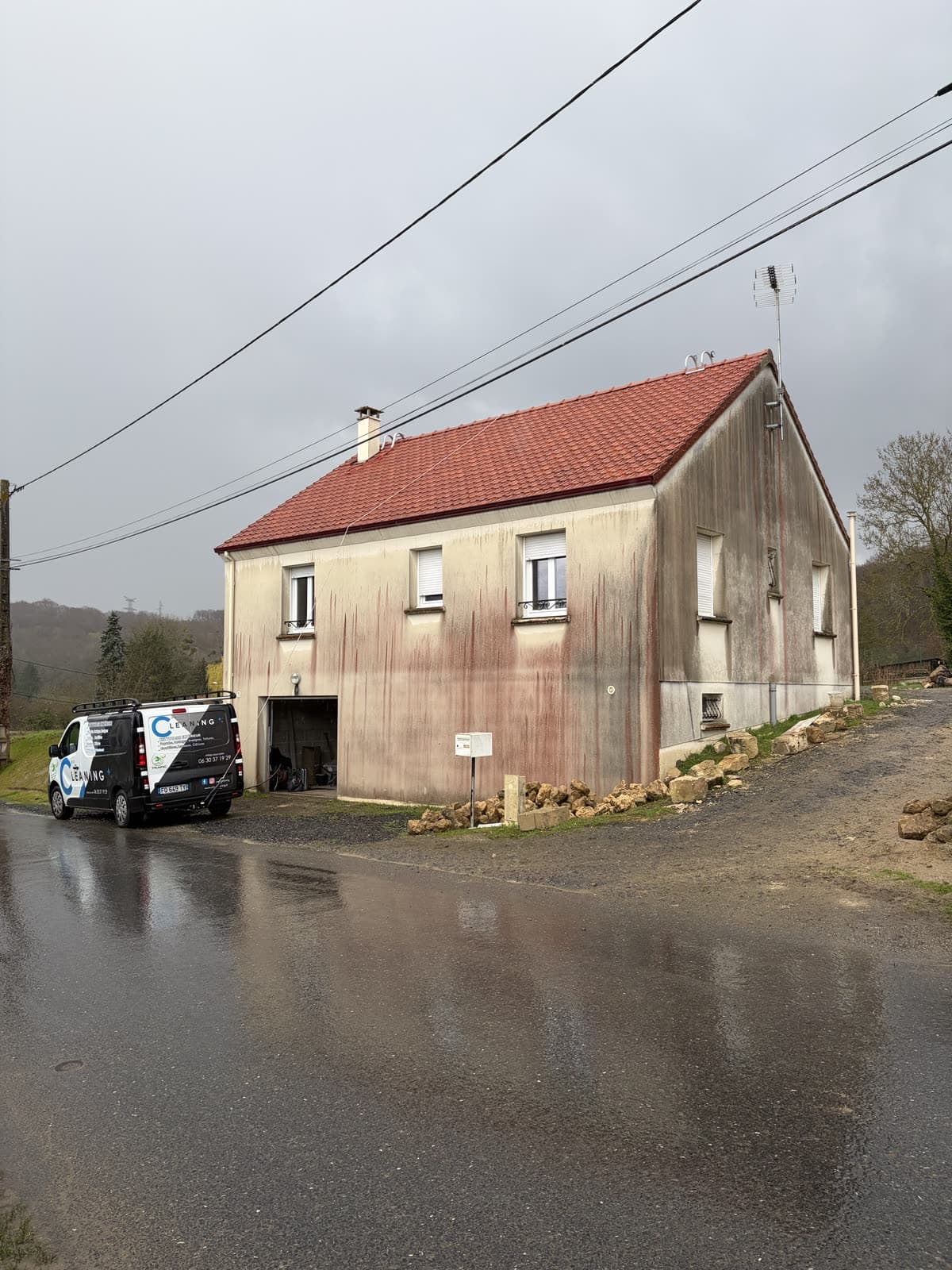 Maison individuelle à l'enduit strié de coulures de rouille, camion Mr Cleaning stationné devant avant l'intervention
