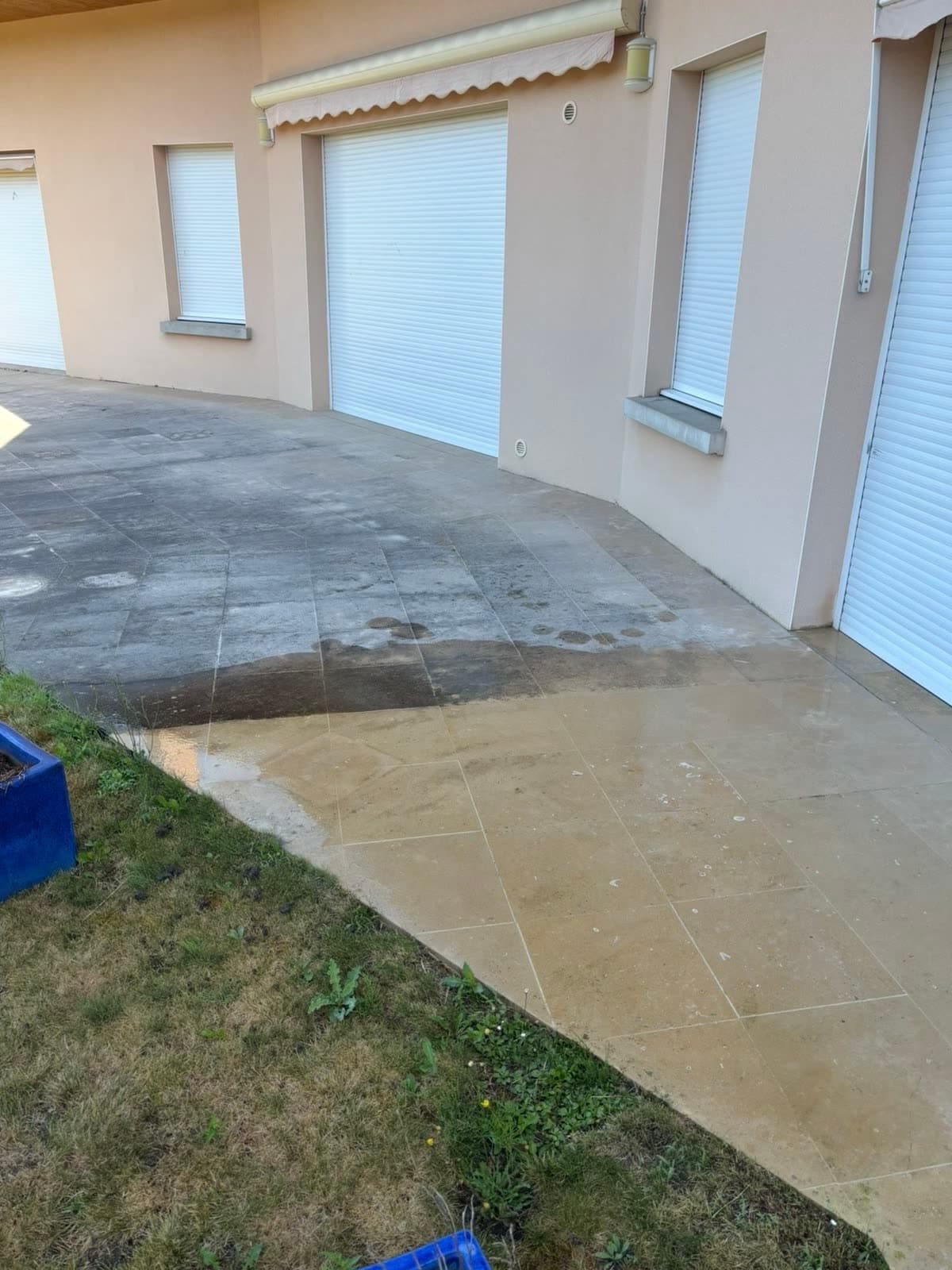 Terrasse en pierre naturelle devant une maison : partie haute encore grise et encrassée, partie basse nettoyée à la teinte sable d'origine