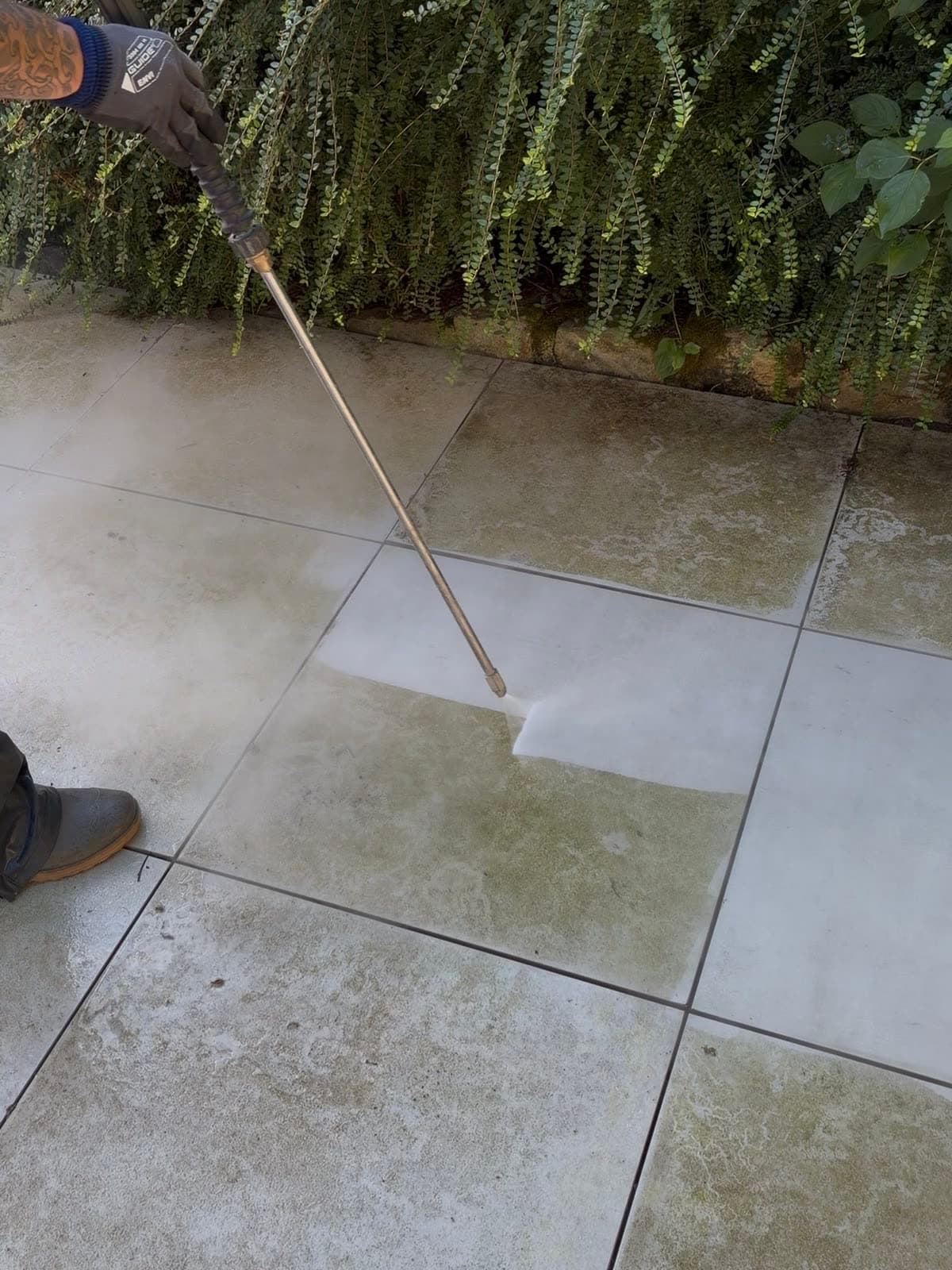 Nettoyage d'une terrasse en carrelage à la lance haute pression : zone claire dégagée au milieu des carreaux encore verdis