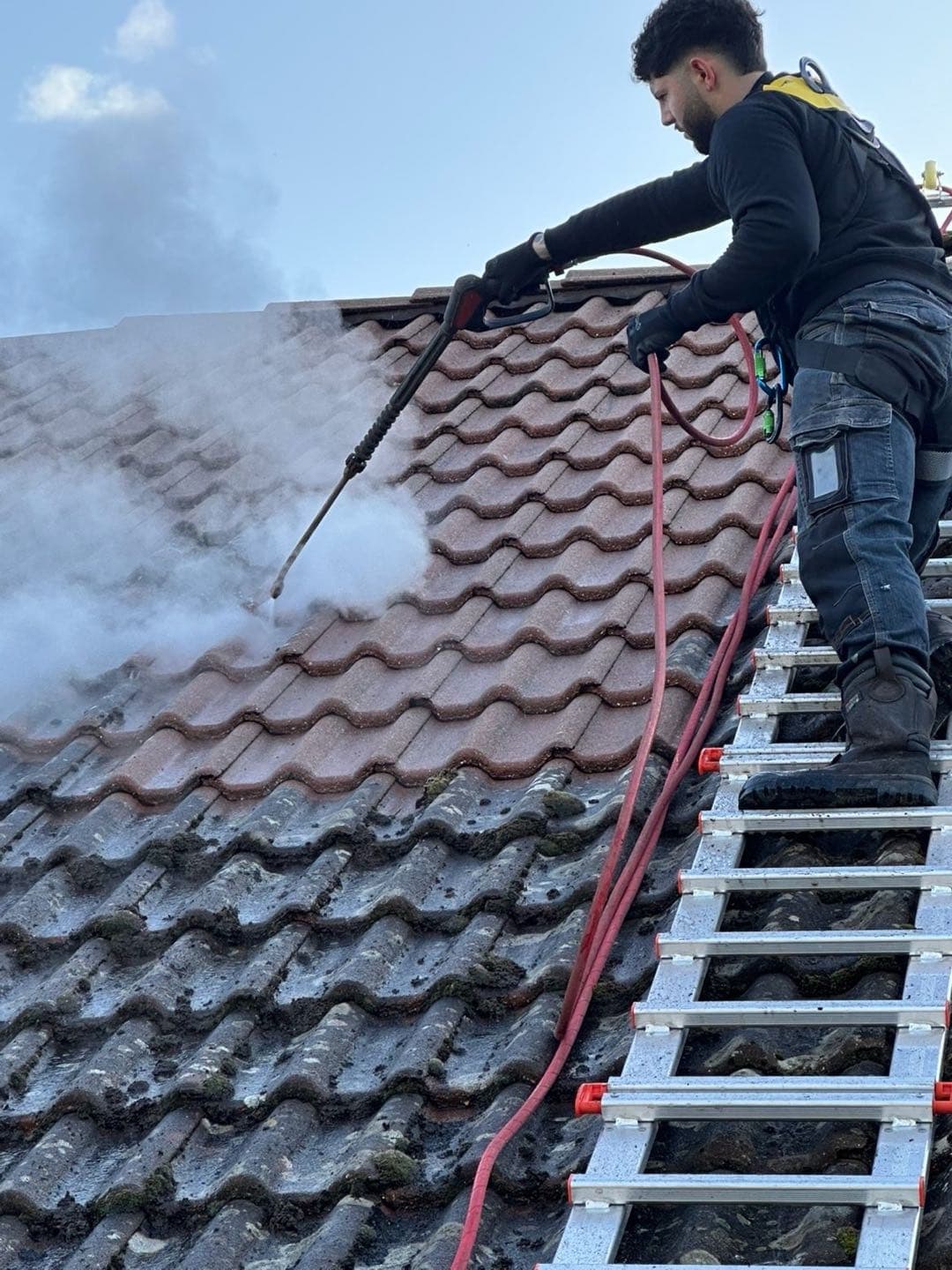 Technicien Mr Cleaning nettoyant une toiture dans l'Aisne : tuiles ravivées en haut, mousses encore présentes en bas