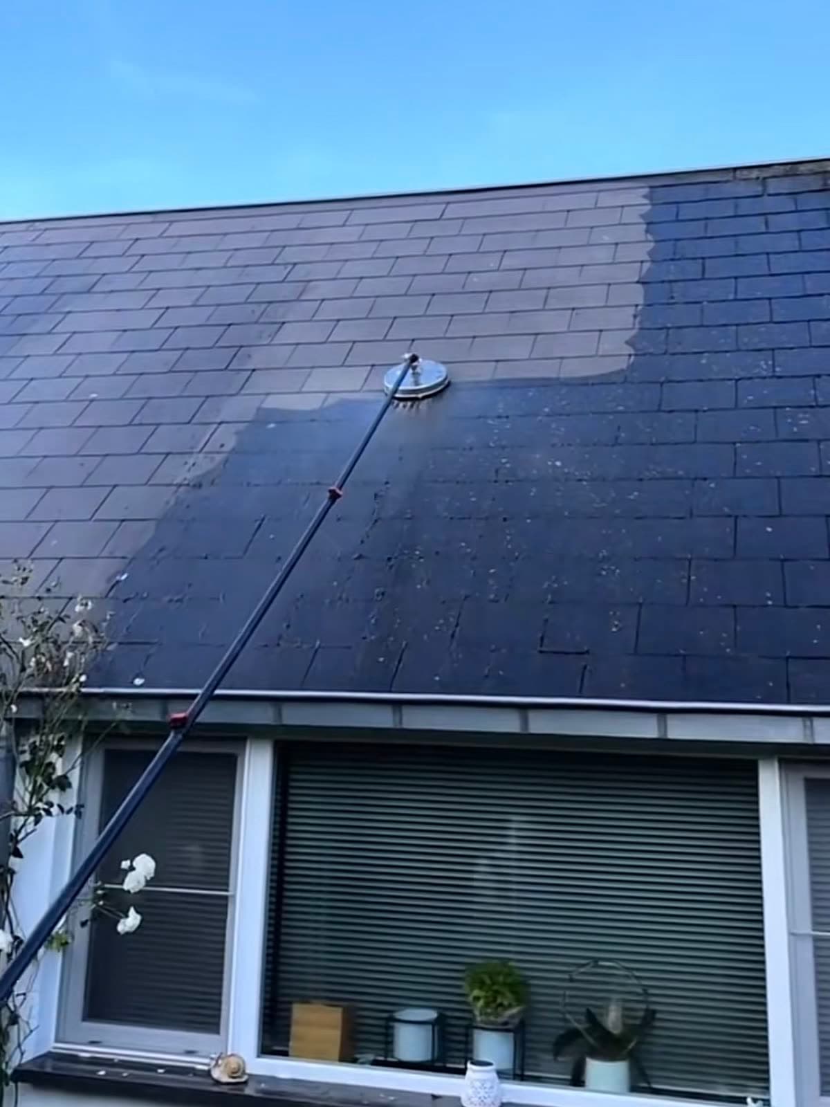 Toiture en ardoise nettoyée à la brosse rotative montée sur perche : la partie traitée a éclairci, le reste de la couverture reste noirci
